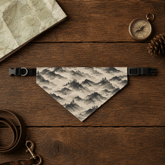 Dog bandana with mountain design on a wooden surface with map, compass, and pine cone.
