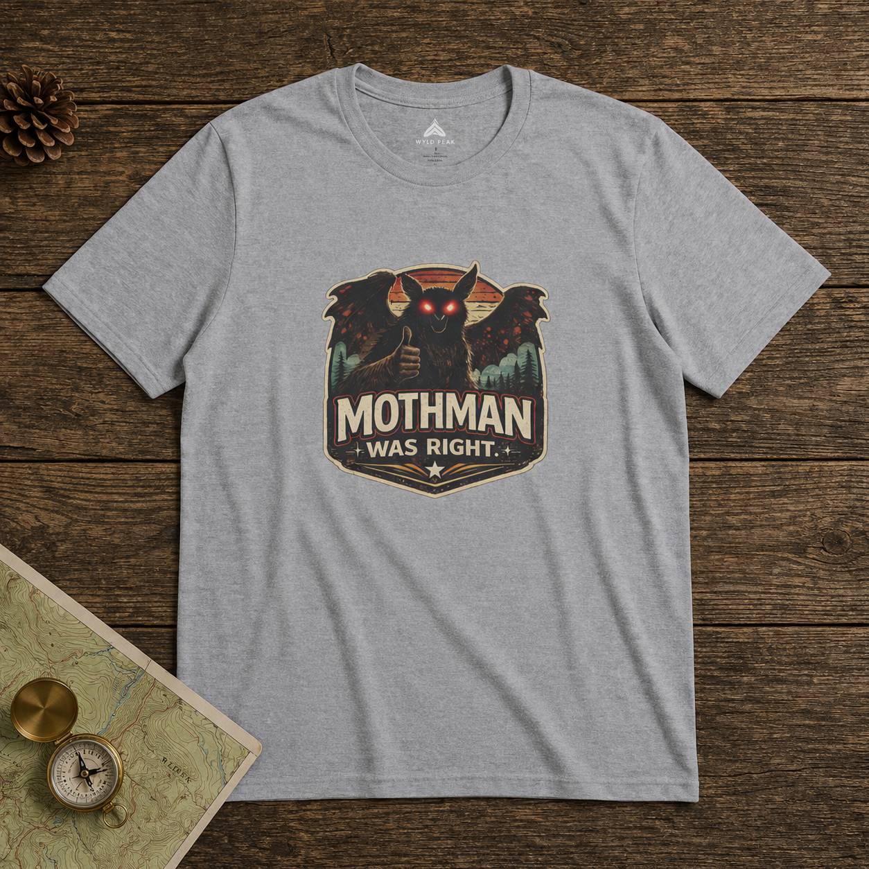 Gray t-shirt with Mothman graphic on a wooden surface