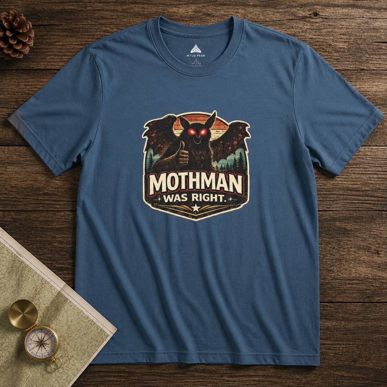 Blue t-shirt with Mothman graphic and 'Mothman Was Right' text on a wooden surface.