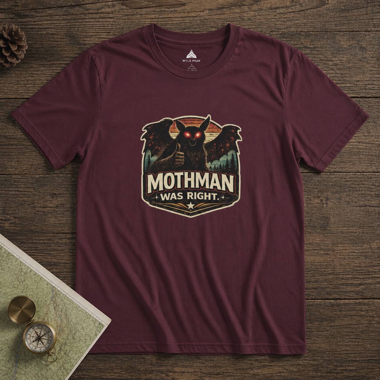 Maroon t-shirt with Mothman graphic and 'Mothman Was Right' text on a wooden surface.