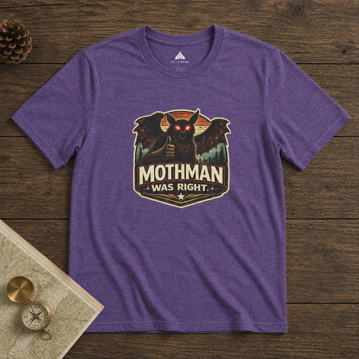 Purple t-shirt with Mothman graphic and 'Mothman Was Right' text on a wooden surface.