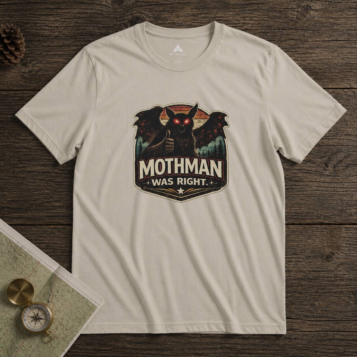 Beige t-shirt with Mothman graphic and 'Mothman Was Right' text on a wooden surface.
