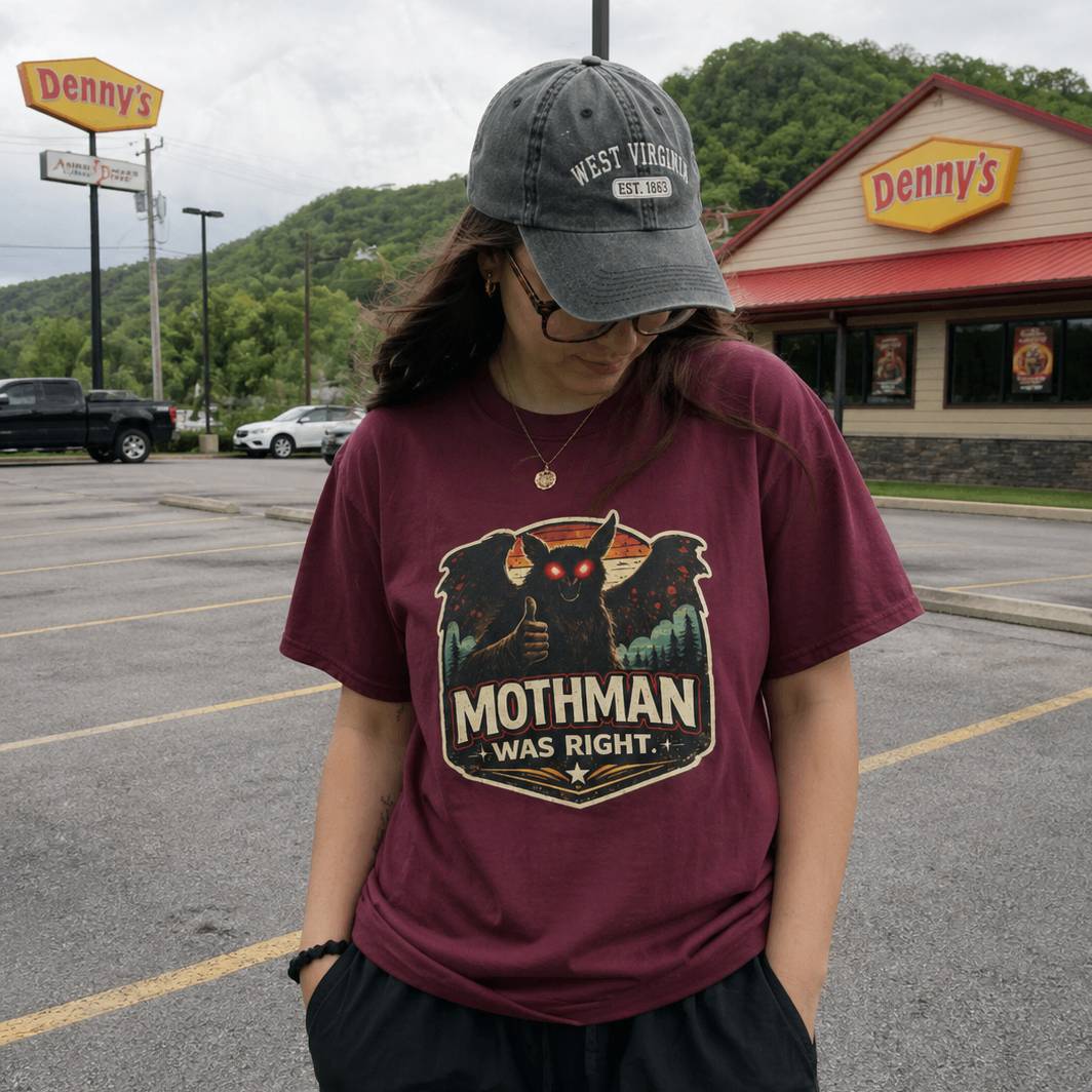 Person wearing a maroon t-shirt with Mothman graphic in front of a Denny's restaurant.