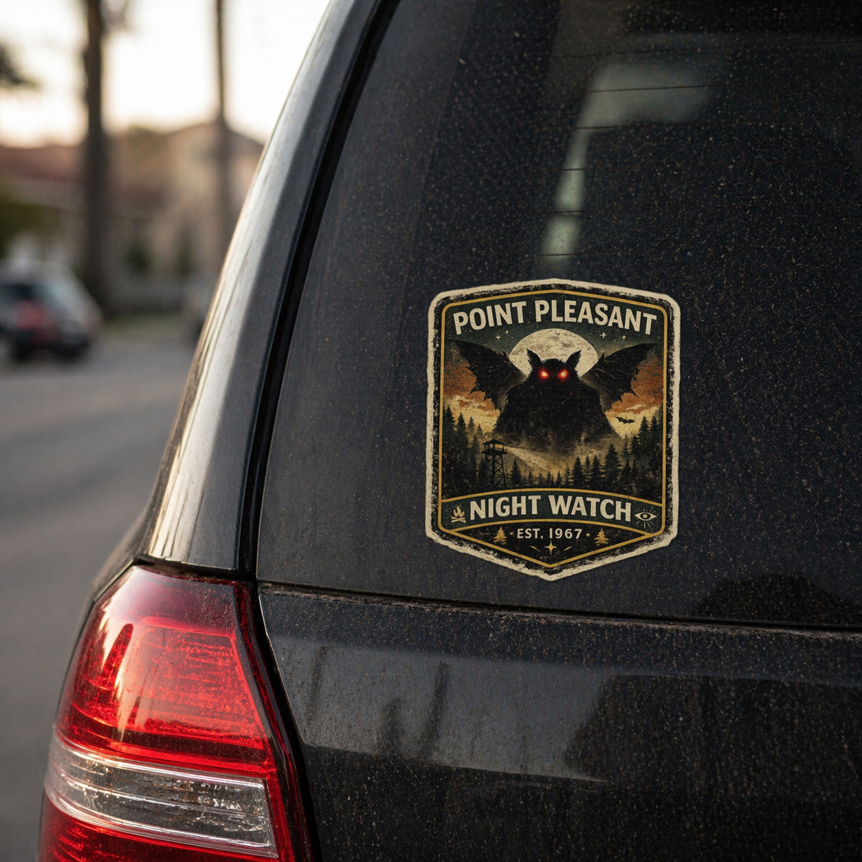 Car sticker with 'Point Pleasant Night Watch' mothman design on a black car.
