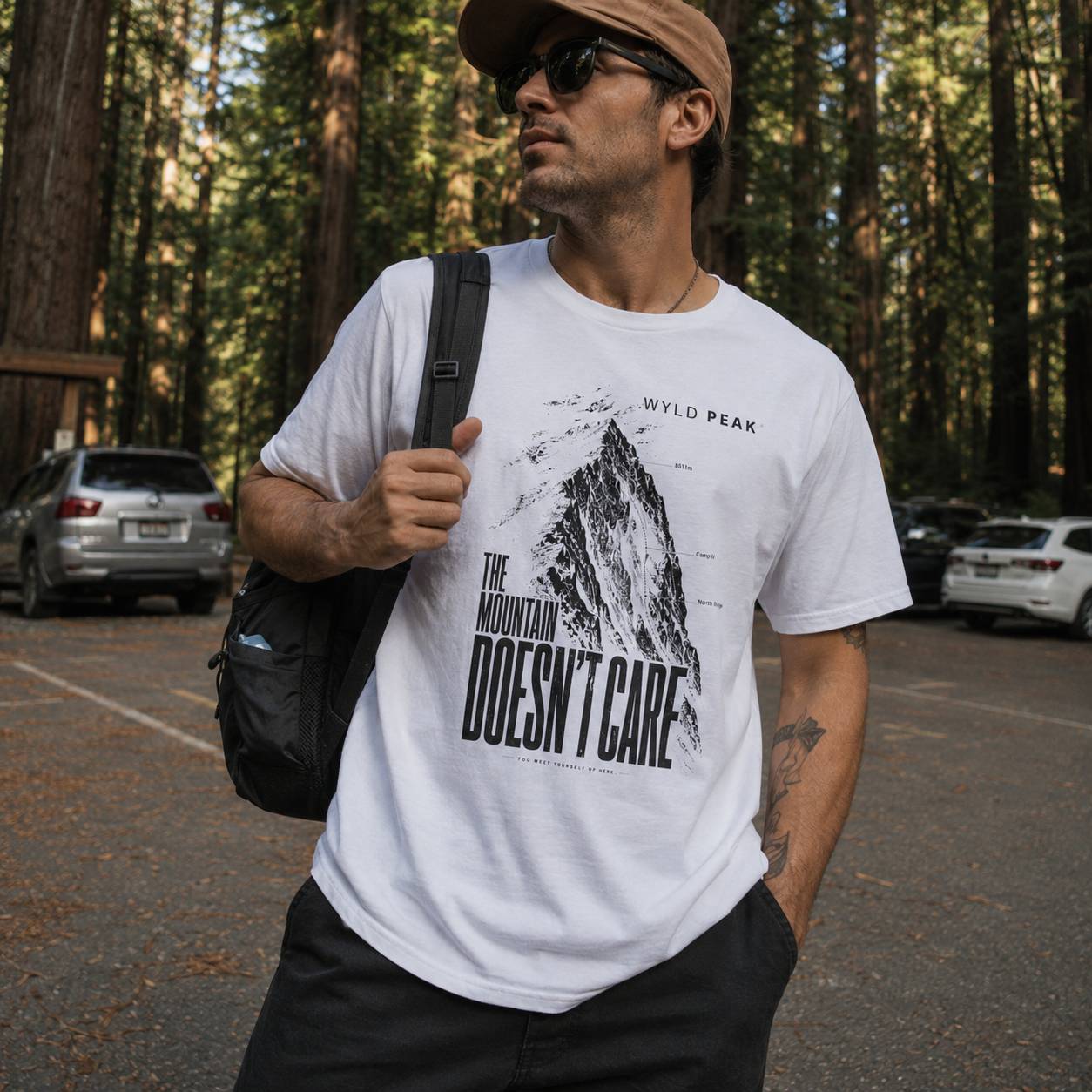 Man wearing a white t-shirt with a mountain graphic and text in a forest setting