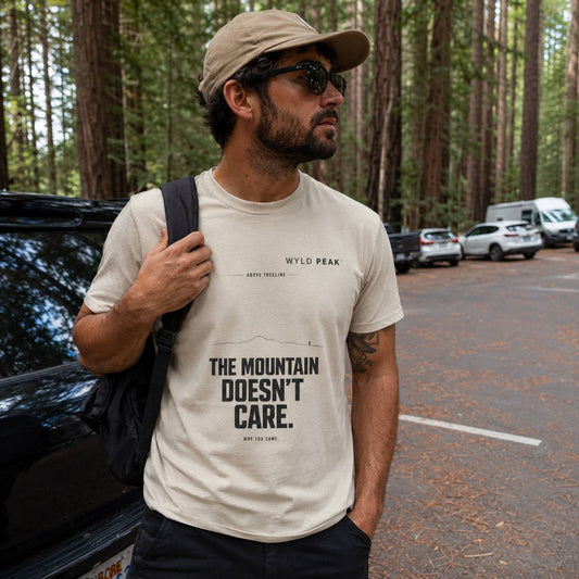 Man wearing a t-shirt with 'The Mountain Doesn't Care' text in a forest setting.