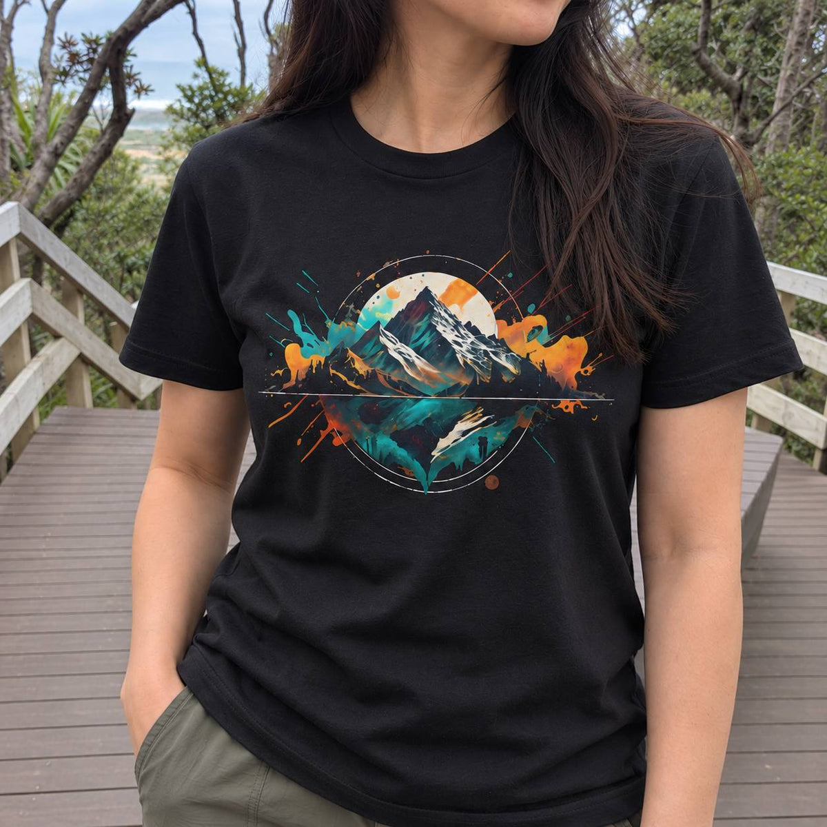 A woman wearing a black short-sleeve graphic t-shirt with a colorful mountain design, standing on a wooden boardwalk outdoors.