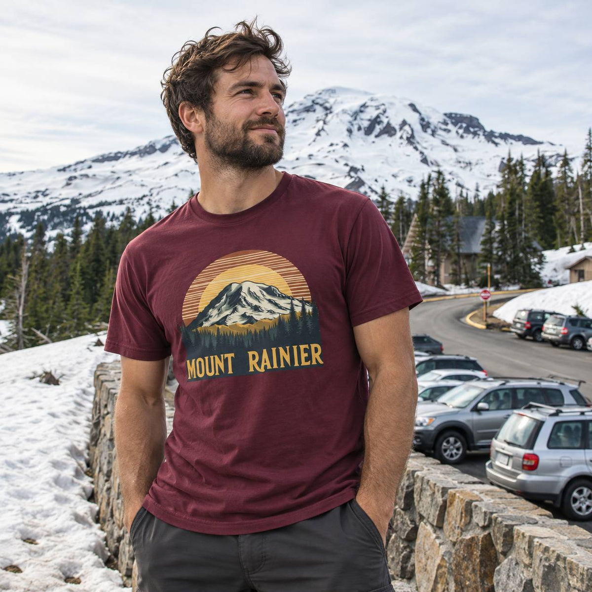 A man wearing a maroon t-shirt with a 'Mount Rainier' graphic, standing outdoors in a snowy mountain setting.