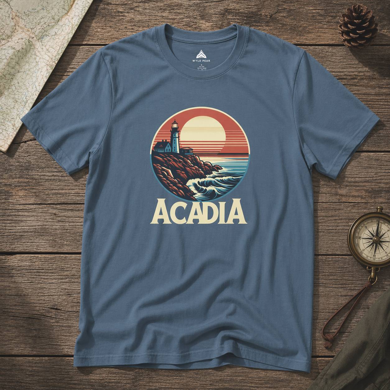 Blue t-shirt with 'Acadia' graphic design on a wooden surface