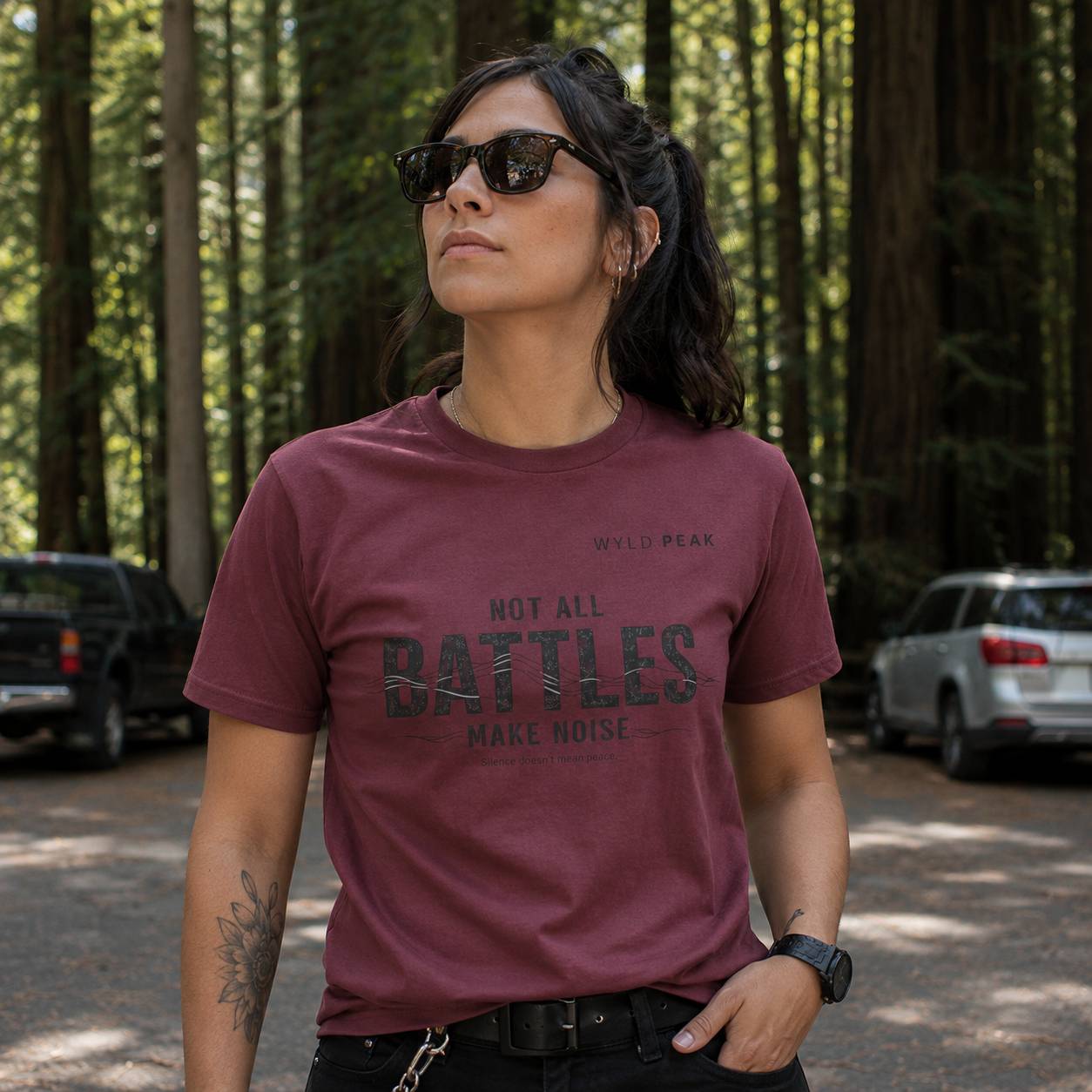Person wearing a maroon t-shirt with text in a forest setting