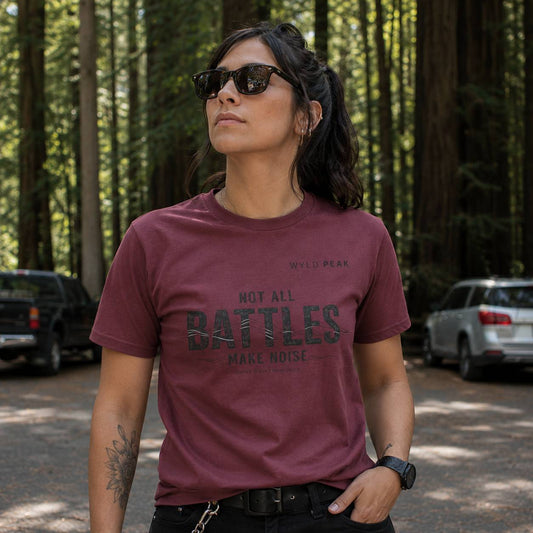 Person wearing a maroon t-shirt with text in a forest setting