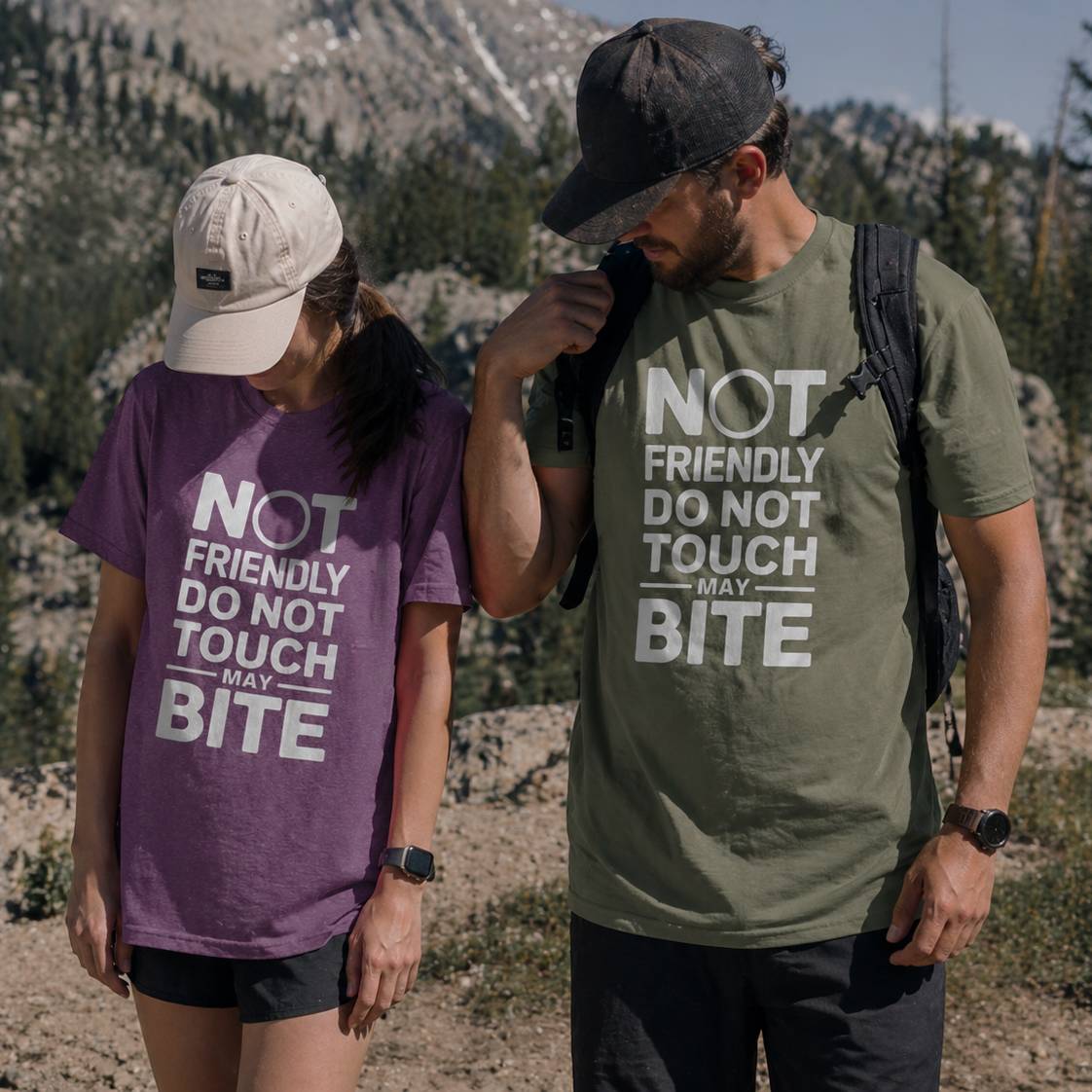 Two people wearing t-shirts with humorous text in a mountainous outdoor setting