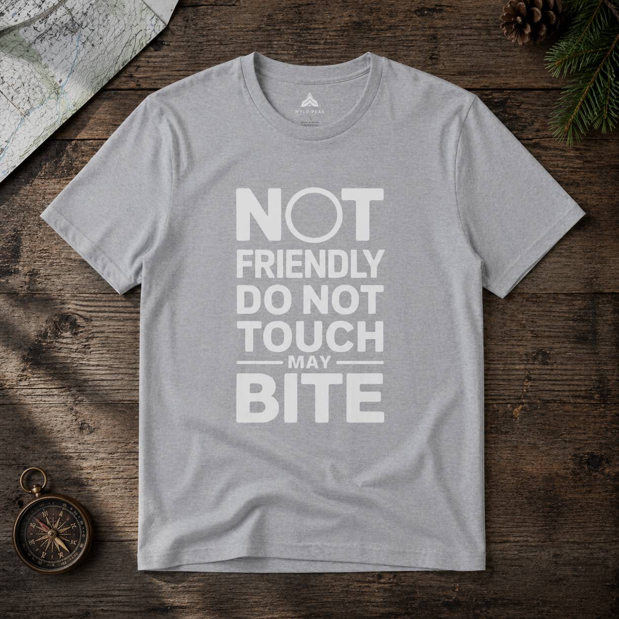 Gray t-shirt with text 'Not friendly do not touch may bite' on a wooden surface.