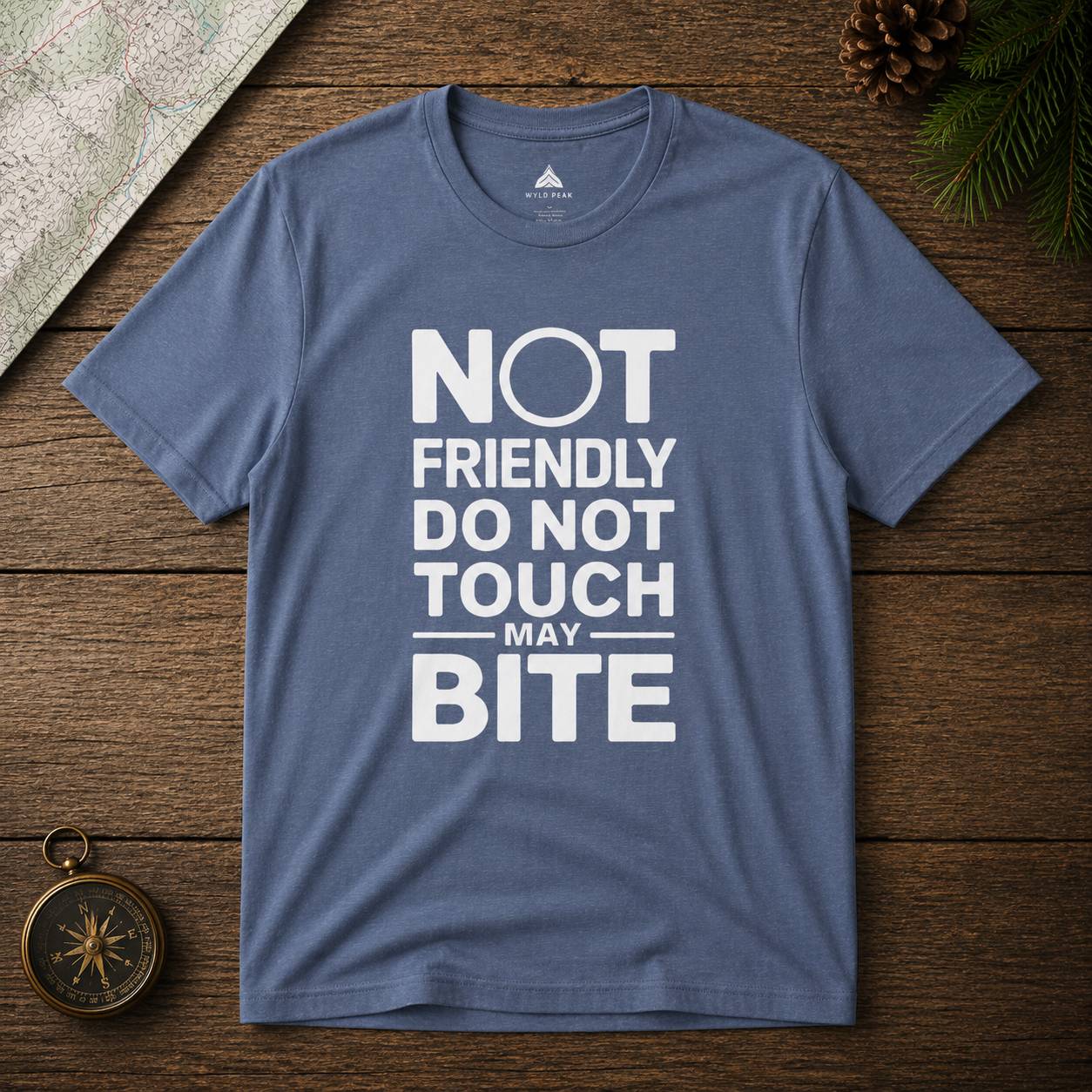 Blue t-shirt with white text 'Not friendly do not touch may bite' on a wooden surface.