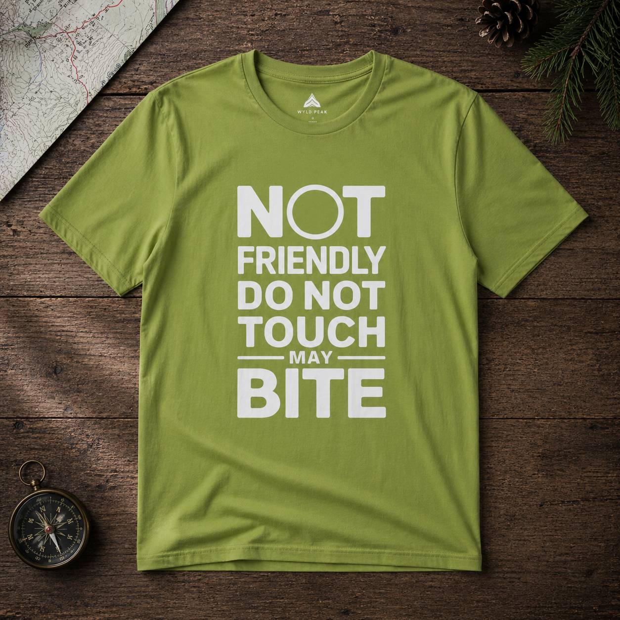 Green t-shirt with text 'Not friendly do not touch may bite' on a wooden surface.