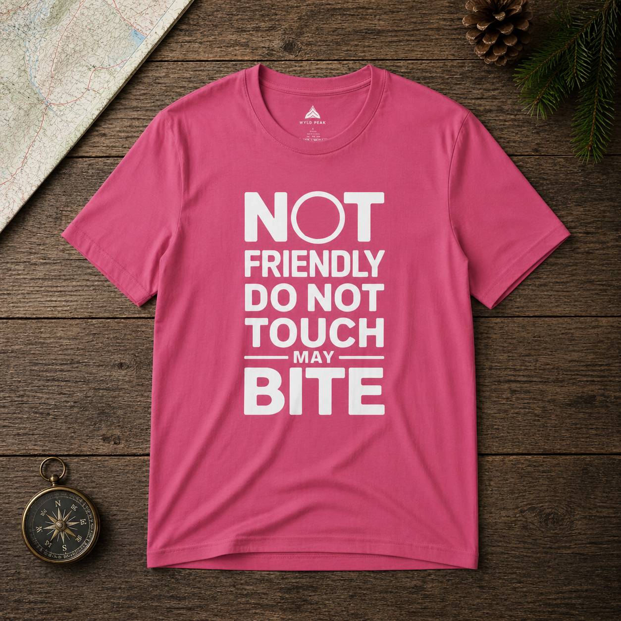 Pink t-shirt with text 'Not friendly do not touch may bite' on a wooden surface.