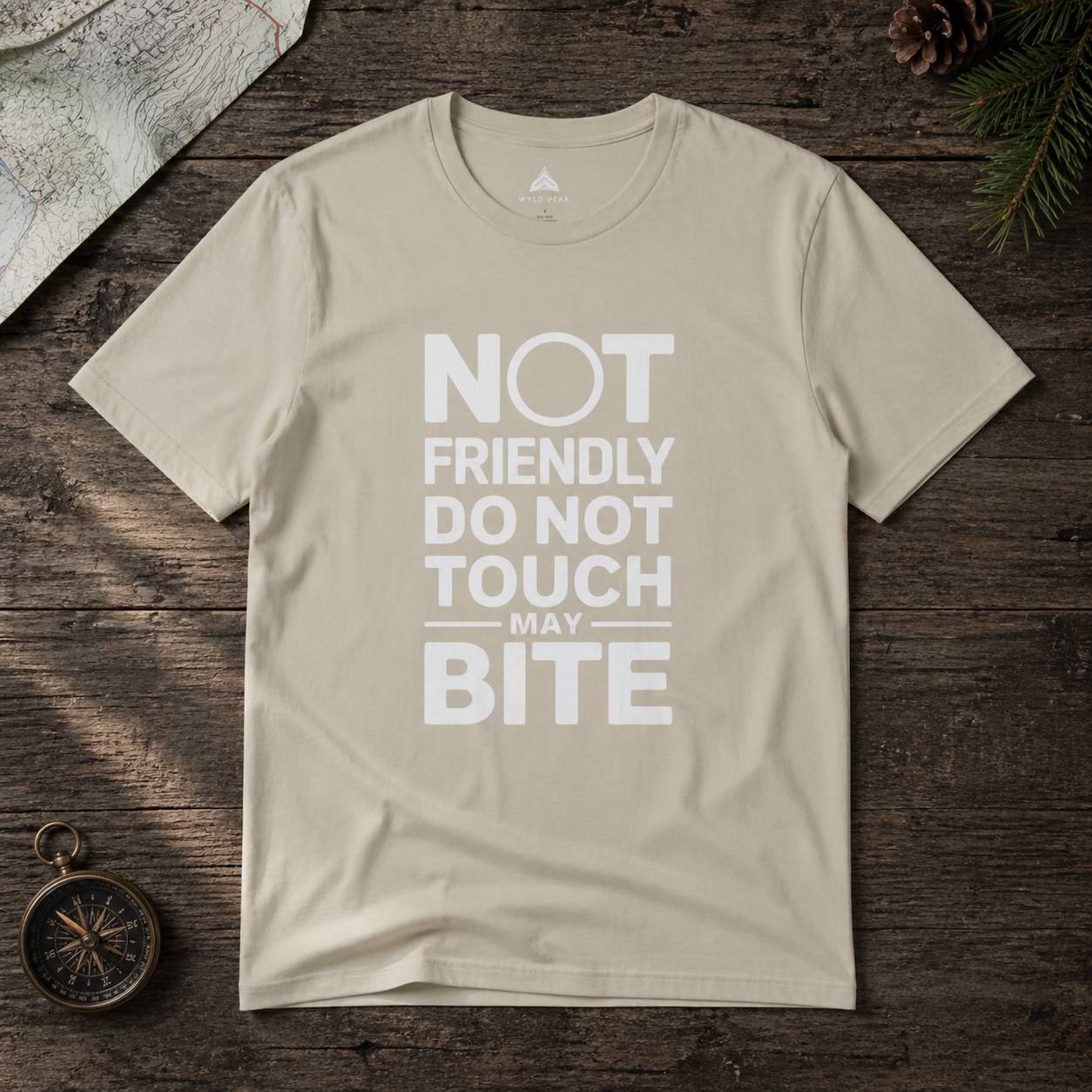 Beige t-shirt with text 'Not friendly do not touch may bite' on a wooden surface.