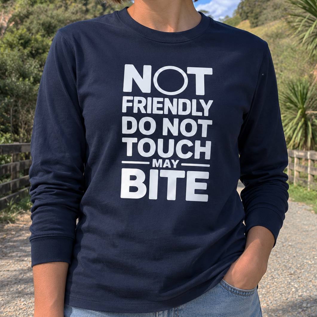 A person wearing a navy blue long-sleeve t-shirt with bold white text that reads 'NOT FRIENDLY DO NOT TOUCH MAY BITE', photographed outdoors on a gravel path with greenery in the background.