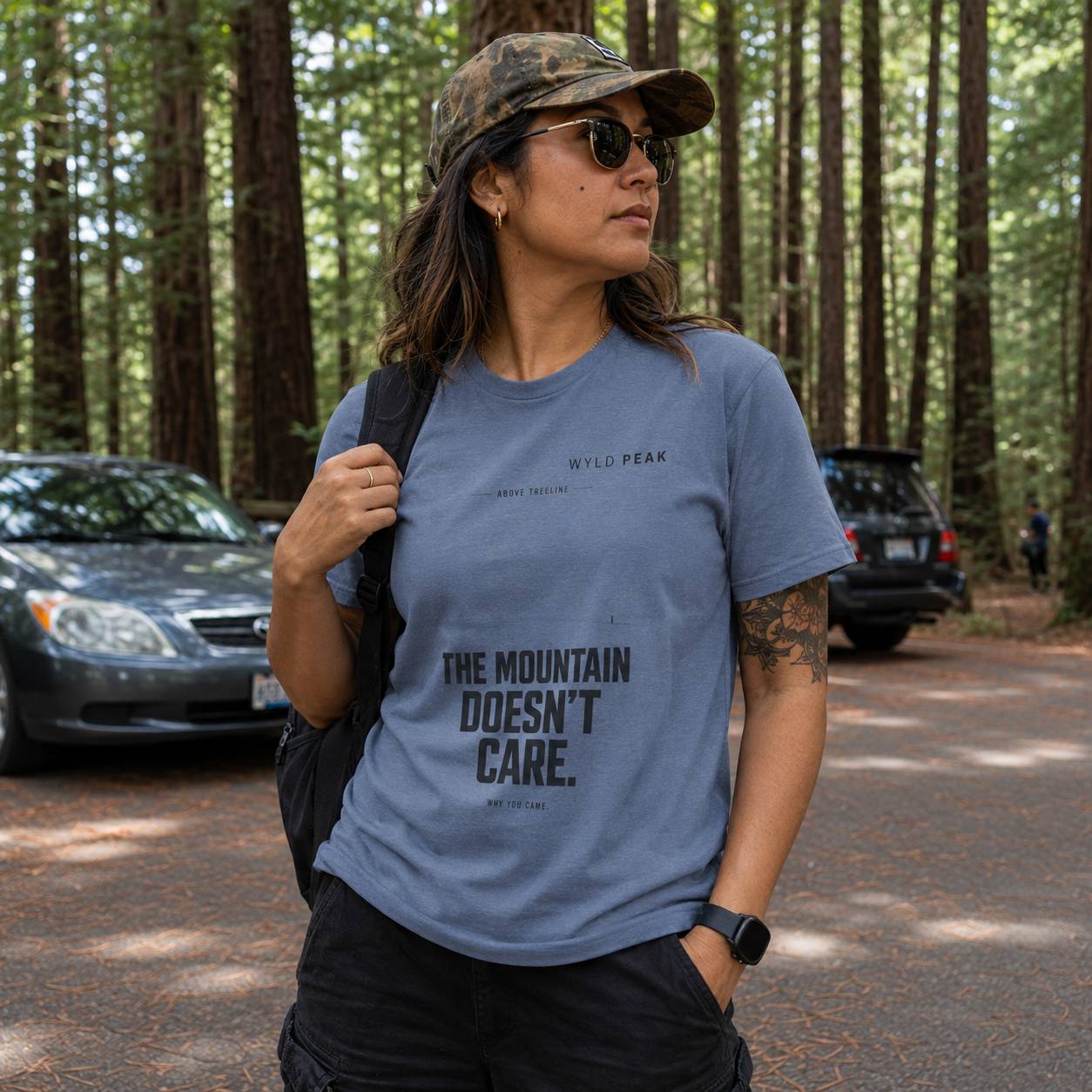 Person wearing a blue t-shirt with 'The Mountain Doesn't Care' text in a forest setting.