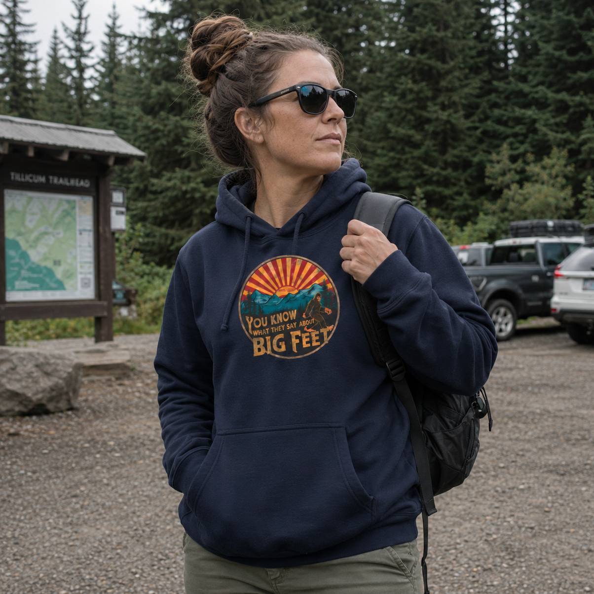 Woman wearing a navy hoodie with a graphic design, standing outdoors near trees and a map.