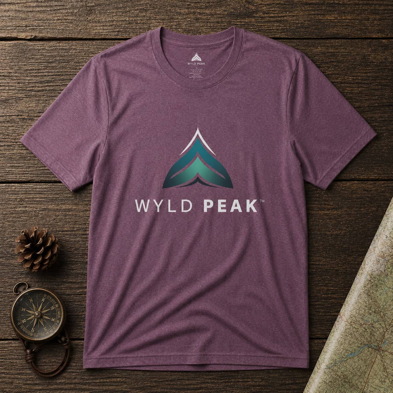 Purple t-shirt with 'WYLD PEAK' logo on a wooden surface with nature-themed items.