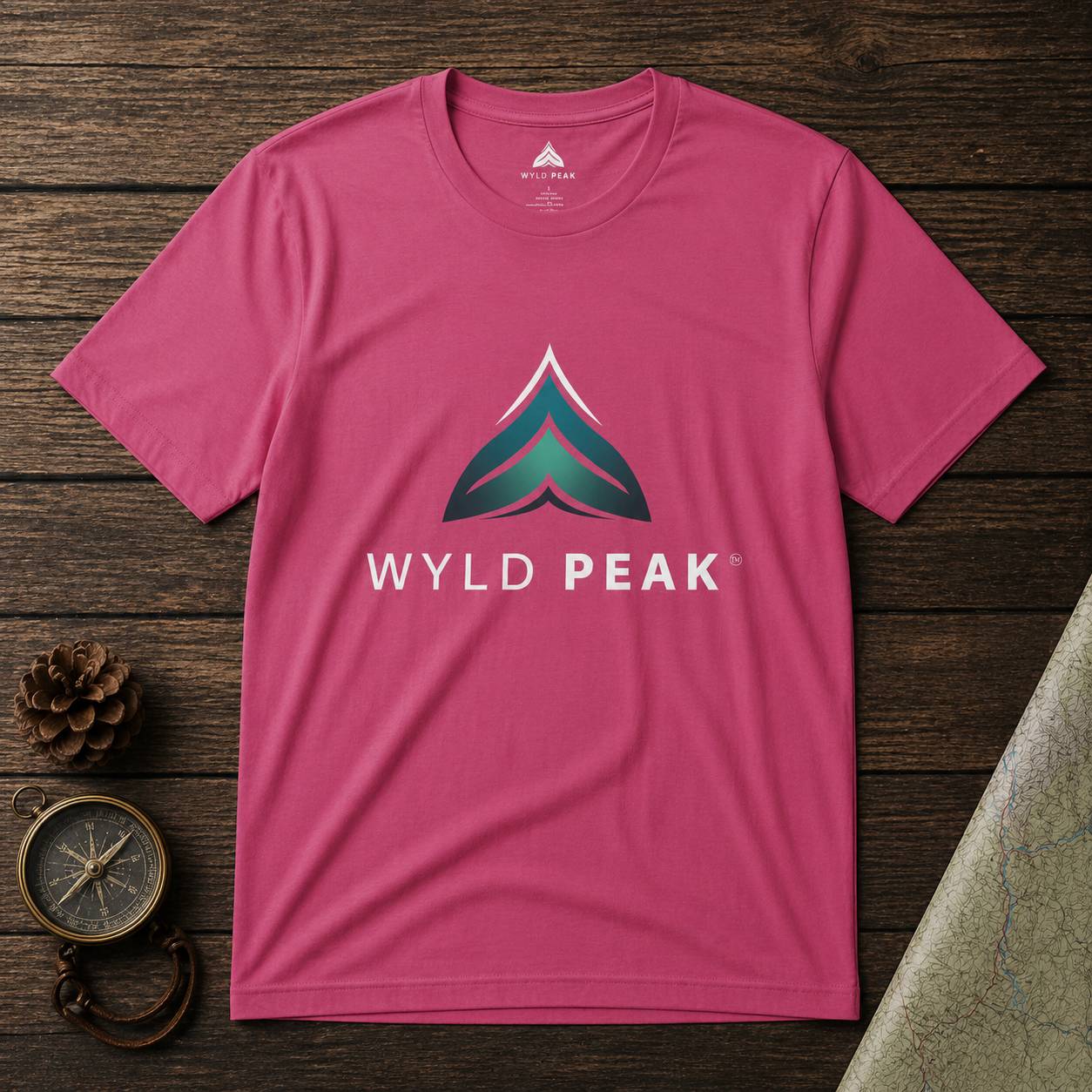 Pink t-shirt with Wyld Peak logo on a wooden surface