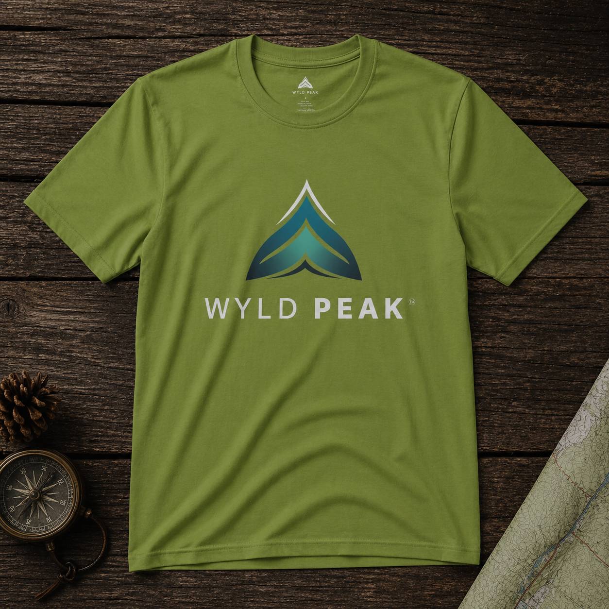 Green t-shirt with Wyld Peak logo on a wooden surface