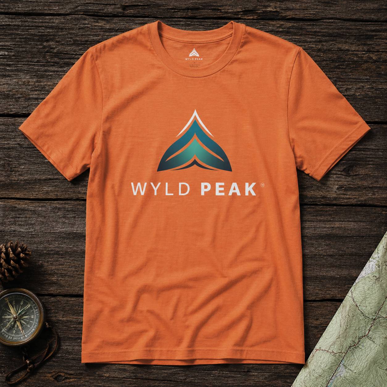 Orange t-shirt with Wyld Peak logo on a wooden surface
