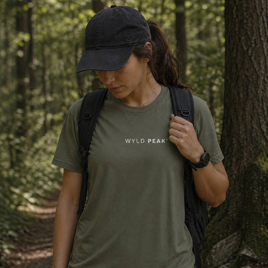 Person wearing a green 'Wyld Peak' t-shirt in a forest setting
