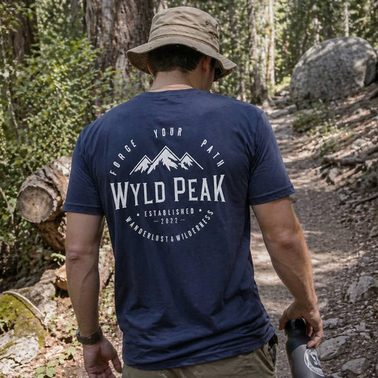 Person wearing a blue 'Wyld Peak' t-shirt in a forest setting