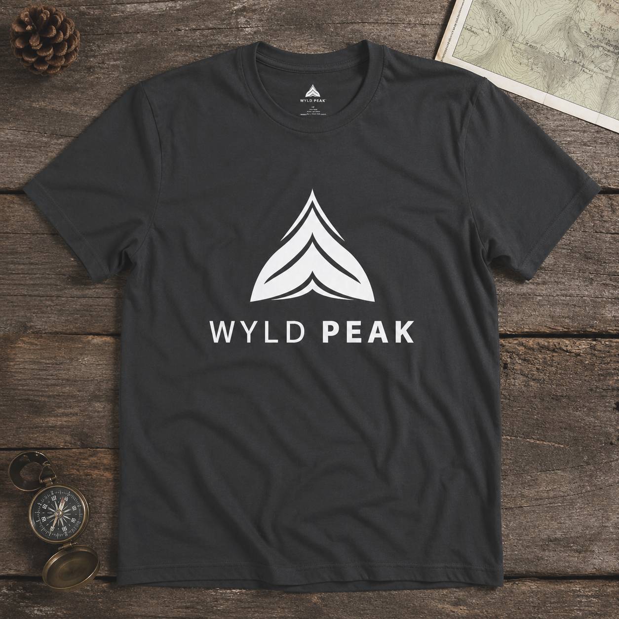 Black t-shirt with 'Wyld Peak' logo on a wooden surface with a map and compass.