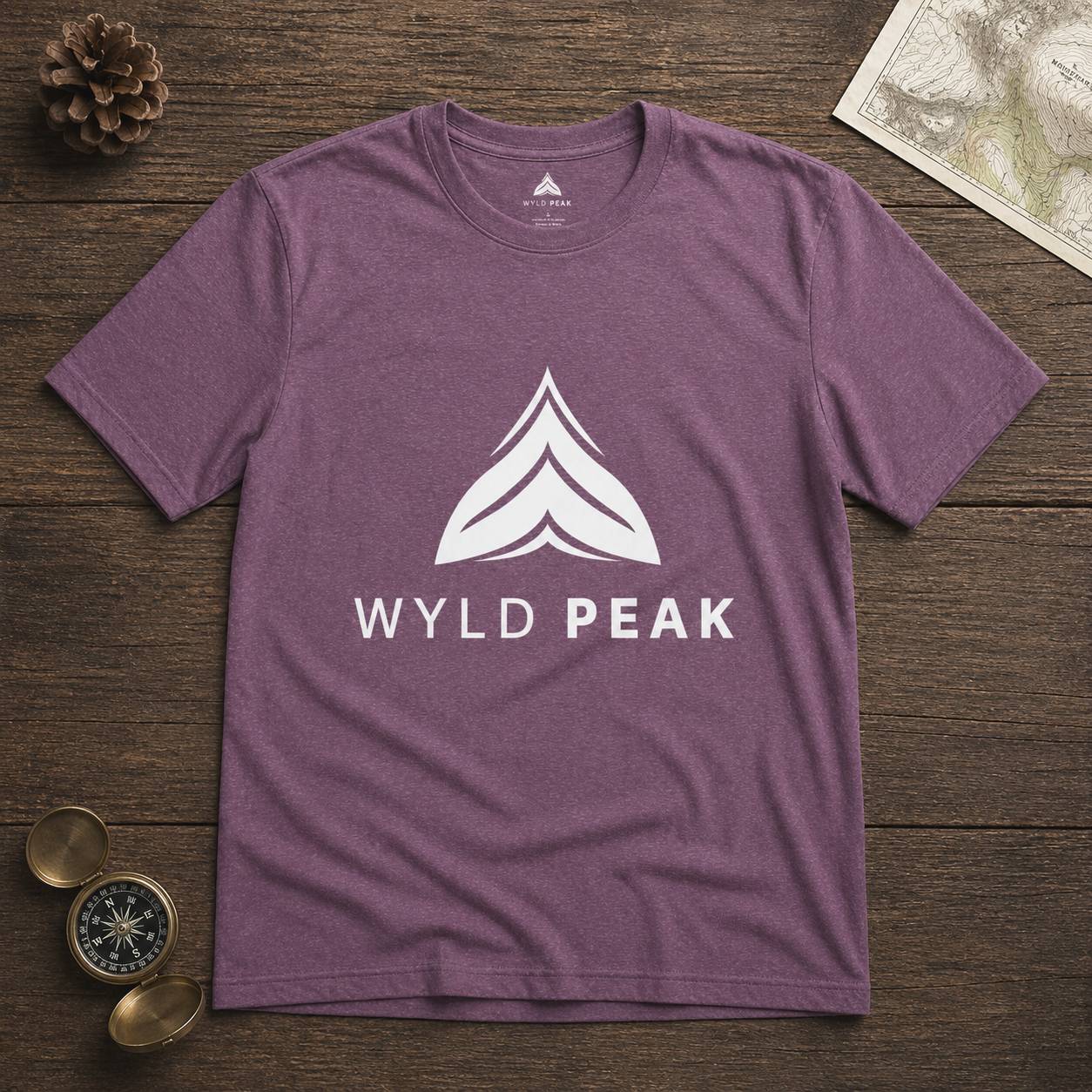 Purple t-shirt with 'Wyld Peak' logo on a wooden surface with map and compass.