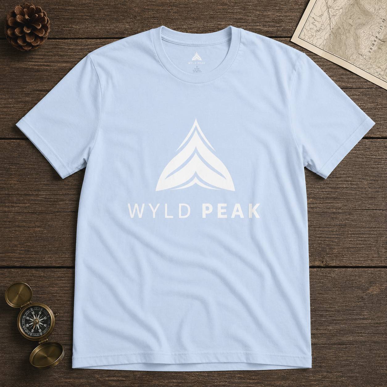 Light blue t-shirt with 'WYLD PEAK' logo on a wooden surface
