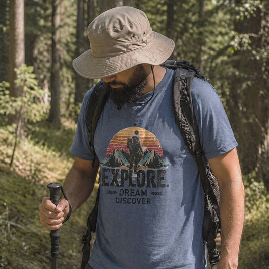 Man hiking in a forest wearing a blue t-shirt with 'Explore. Dream Discover' and mountain graphic.