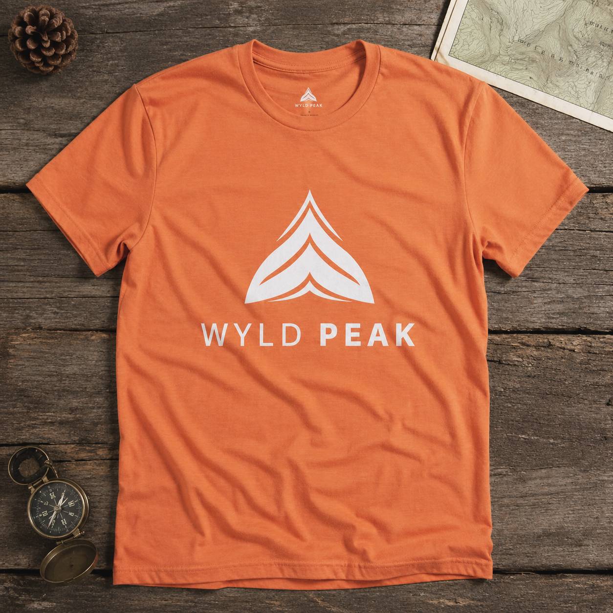 Orange t-shirt with 'Wyld Peak' logo on a wooden surface