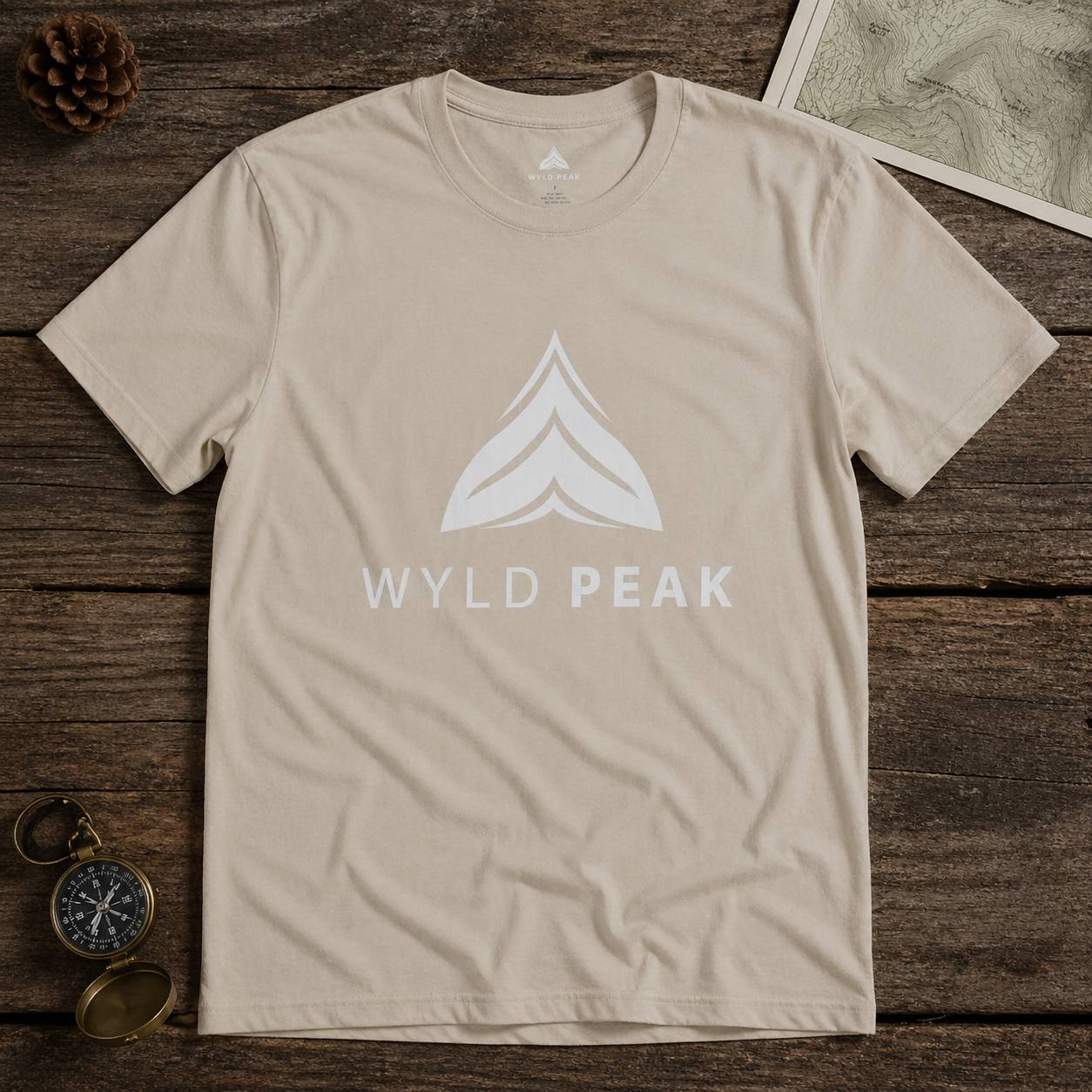 Beige t-shirt with 'Wyld Peak' logo on a wooden surface
