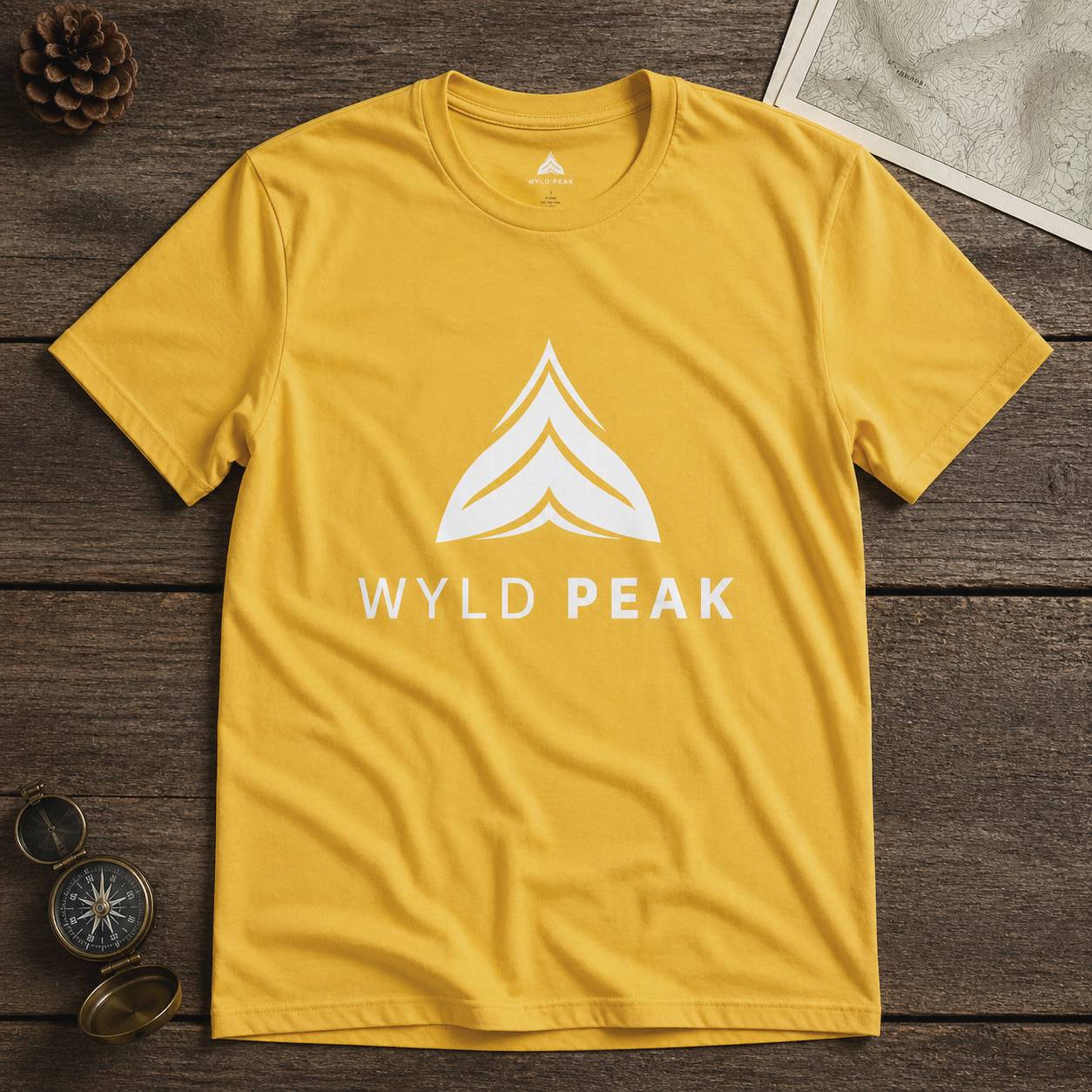 Yellow t-shirt with 'WYLD PEAK' logo on a wooden surface