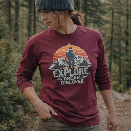 Person wearing a maroon long-sleeve shirt with an 'Explore Dream Discover' graphic in a forest setting