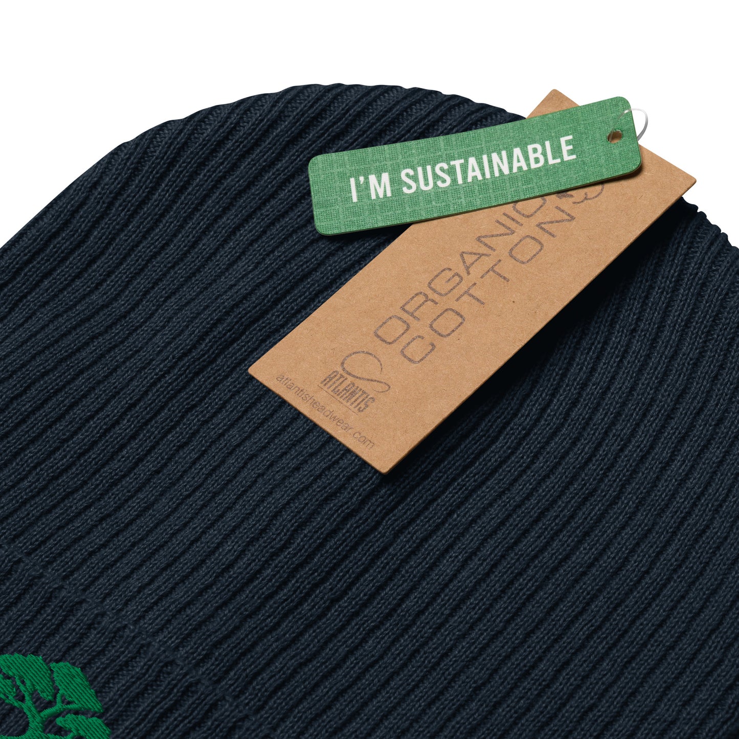 Close-up of a dark navy ribbed knit beanie with a green 'I'M SUSTAINABLE' tag and a brown paper 'ORGANIC COTTON' tag from Planty's, on a white background.