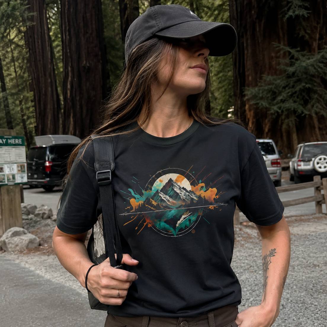 Person wearing a black t-shirt with a mountain graphic in a forest setting