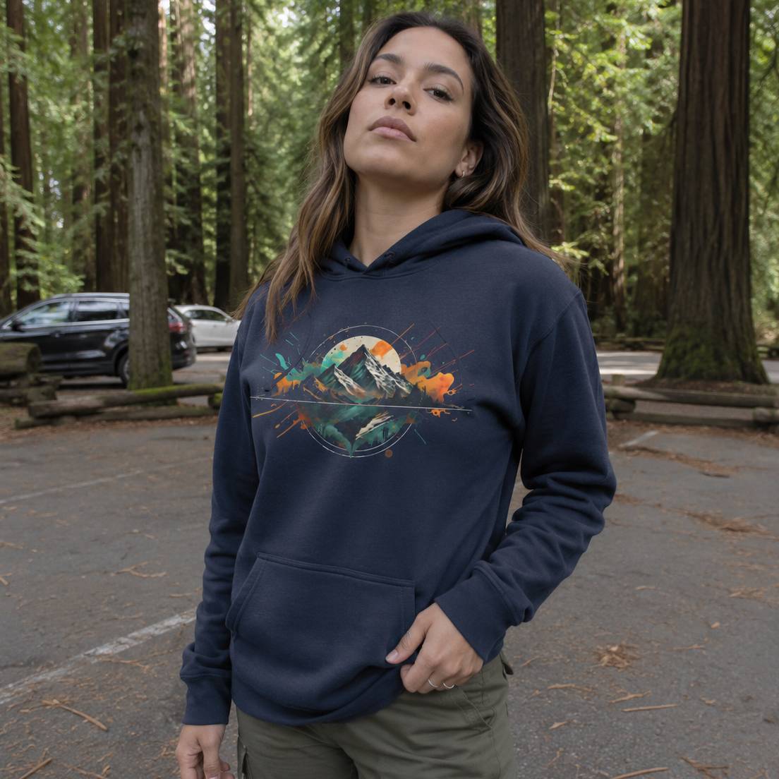 Woman wearing a navy blue hoodie with a mountain graphic in a forest setting