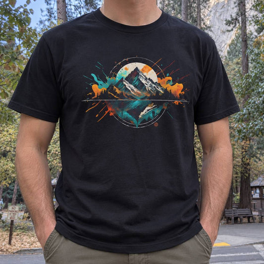 A man wearing a black short-sleeve t-shirt with a colorful graphic print of mountains, deer, and a sun, photographed outdoors in a park setting.