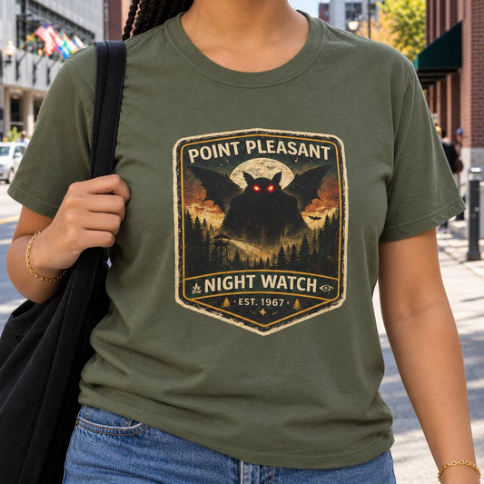 A woman wearing an olive green graphic t-shirt with a 'Point Pleasant Night Watch' design, standing on a city street.