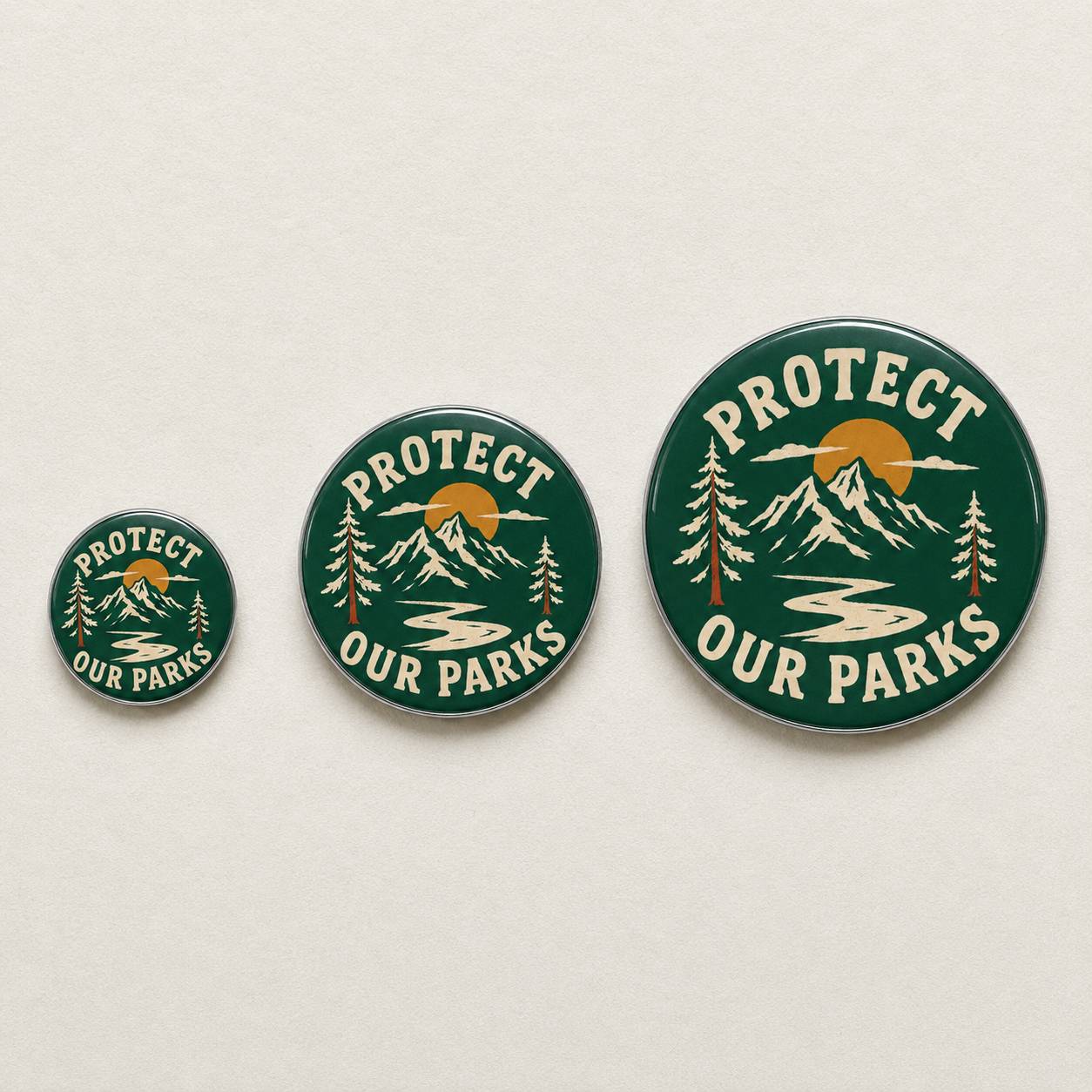 Three round pin-back buttons in ascending sizes featuring a dark green landscape design with mountains, pine trees, a winding river, and a yellow-orange sun, with the text 'PROTECT OUR PARKS' in cream lettering.