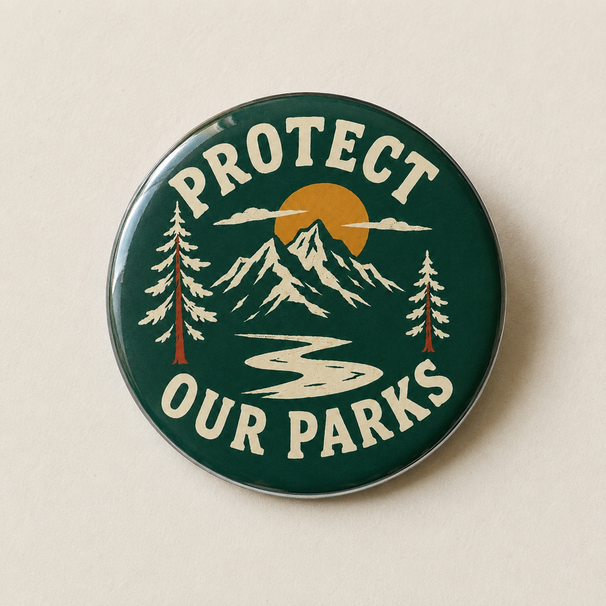 A round enamel pin with a dark green background featuring a mountain landscape, pine trees, a yellow sun, and the text 'PROTECT OUR PARKS' in cream lettering, shown on a light beige background.