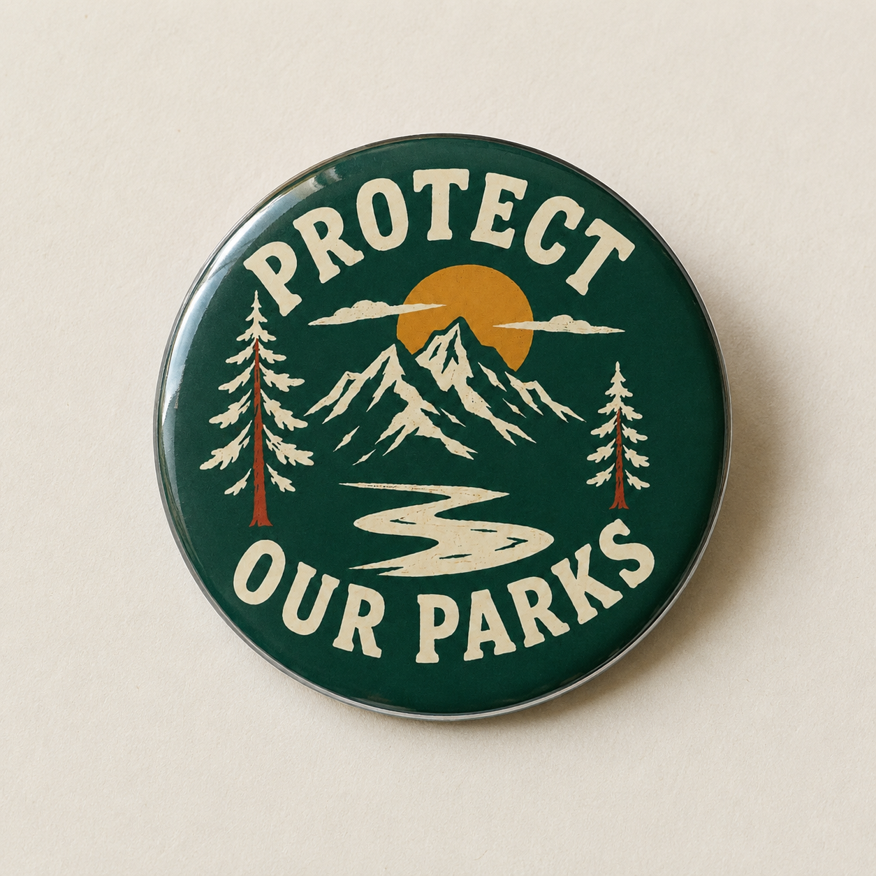 A round enamel pin with a dark green background featuring a mountain landscape, pine trees, a yellow sun, and the text 'PROTECT OUR PARKS' in cream lettering, shown on a light beige background.
