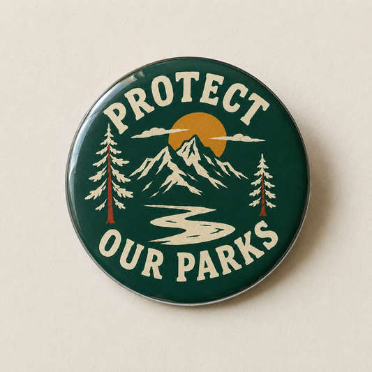 A round enamel pin with a dark green background featuring a mountain landscape, pine trees, a yellow sun, and the text 'PROTECT OUR PARKS' in cream lettering, shown on a light beige background.