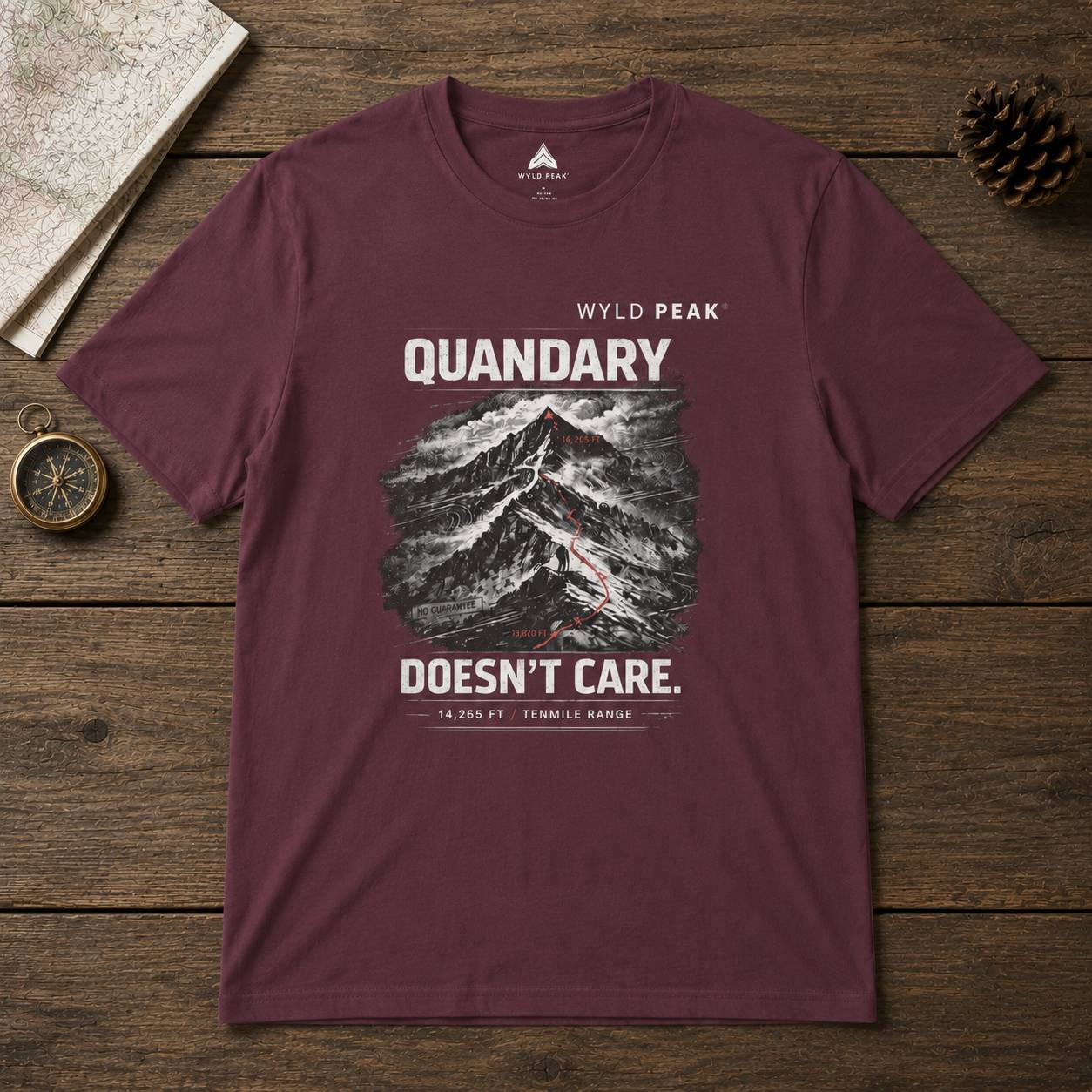 Maroon t-shirt with mountain graphic and text on a wooden surface