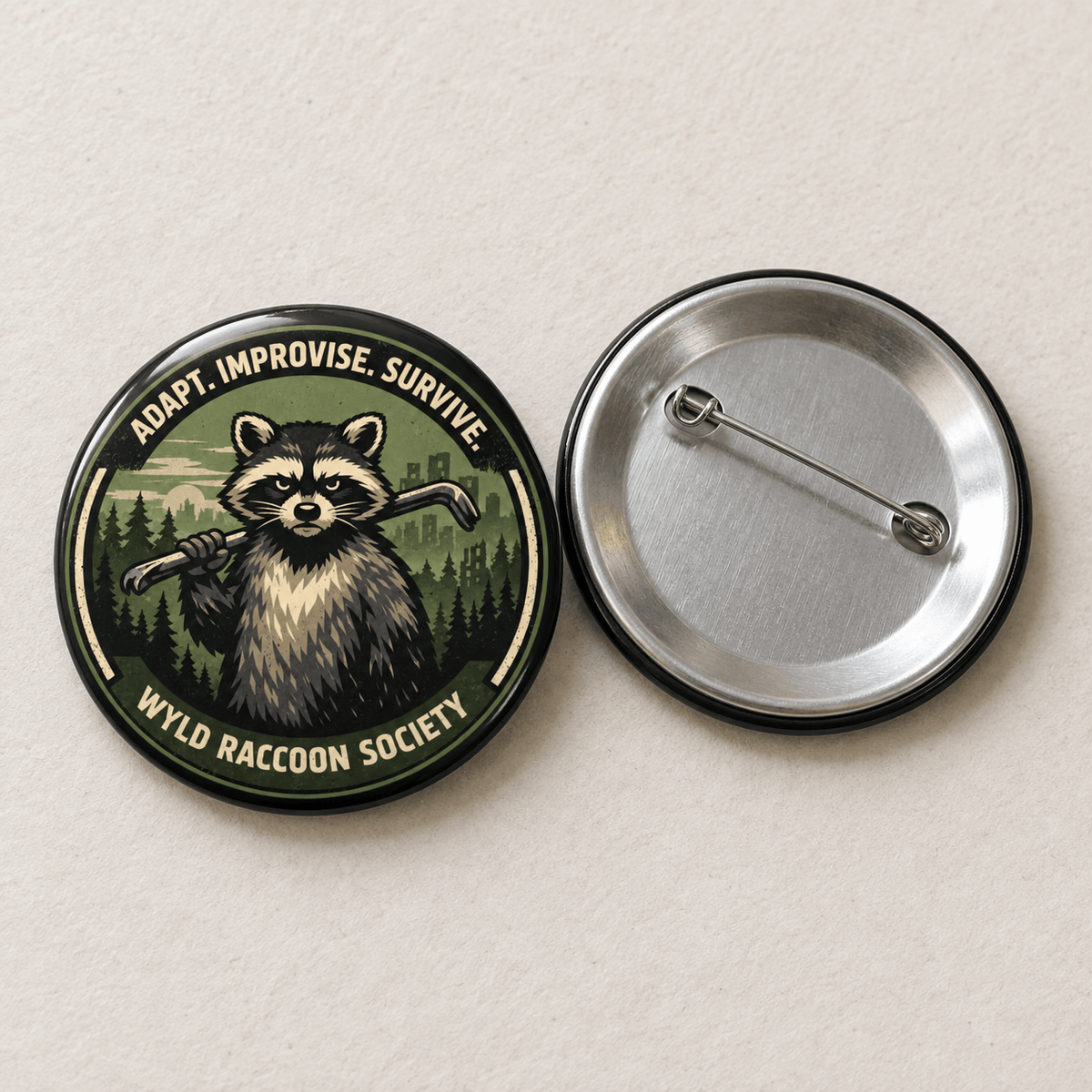 Two round pinback buttons on a light beige textured background. The left button shows a raccoon holding an axe with the text 'ADAPT.