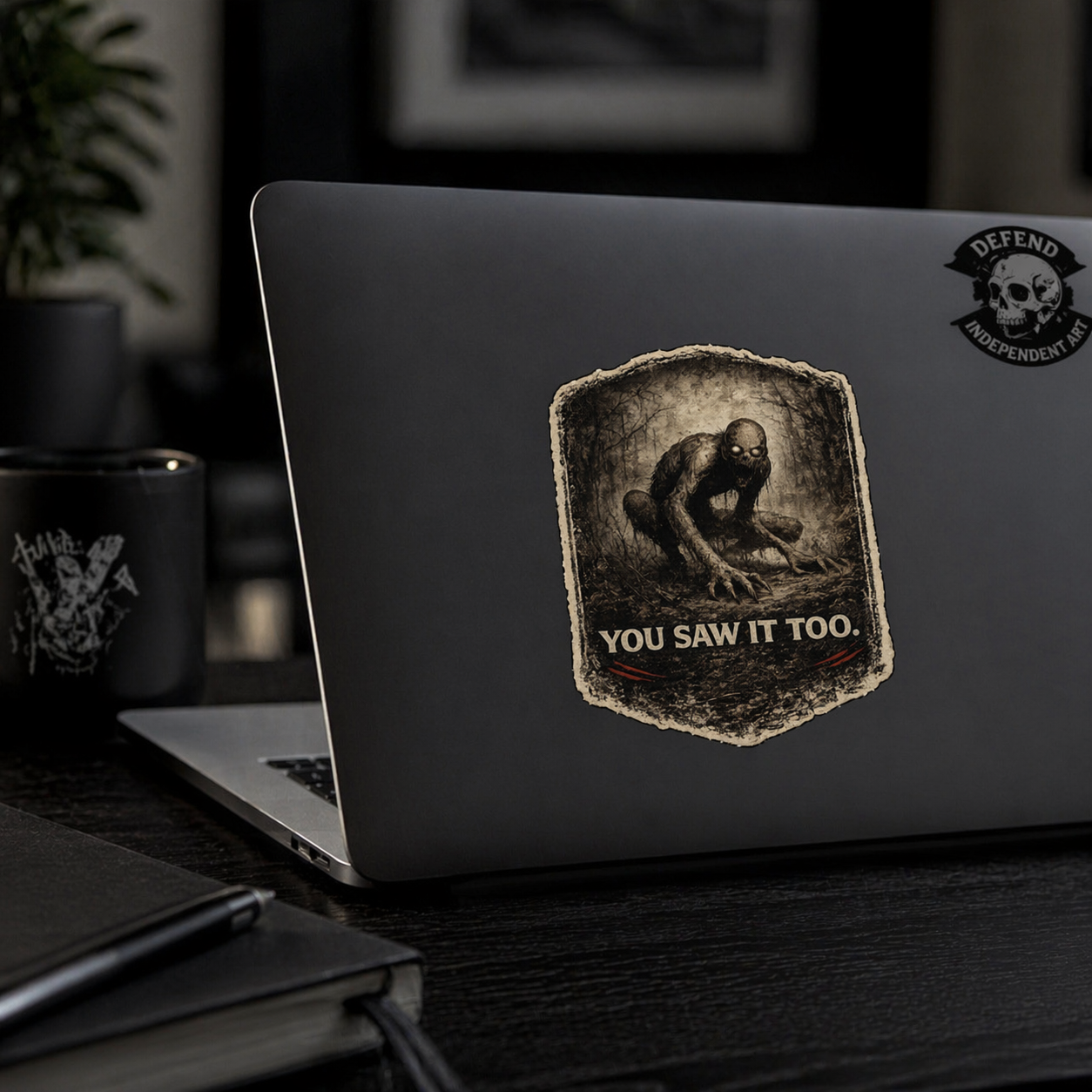 Minimal laptop setup with Rake creepypasta sticker, dark aesthetic horror creature design with moody lighting for eerie and alternative style